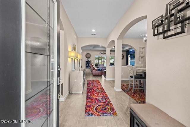 entrance foyer with arched walkways, visible vents, baseboards, and wood finish floors