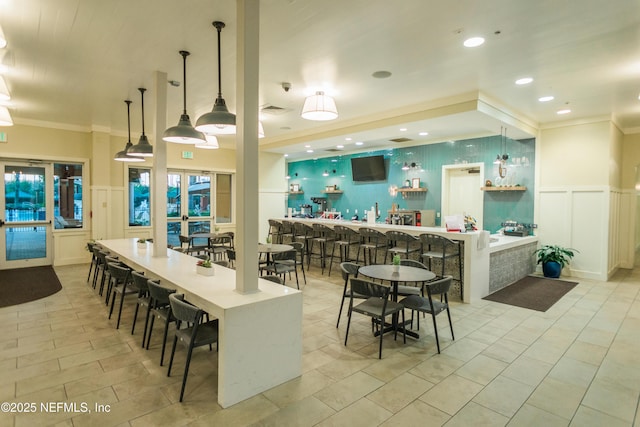kitchen featuring a decorative wall, ornamental molding, pendant lighting, a kitchen bar, and wainscoting