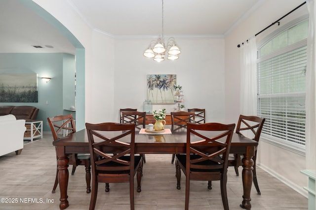 dining room featuring arched walkways, ornamental molding, wood finished floors, baseboards, and a chandelier
