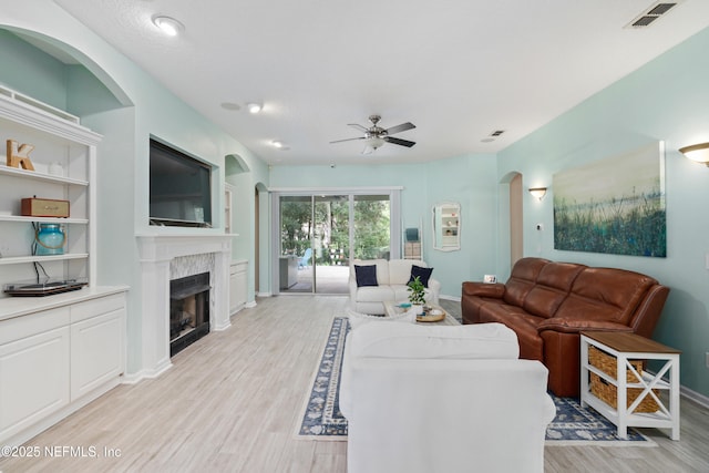 living area with a ceiling fan, light wood-style floors, a fireplace, arched walkways, and baseboards