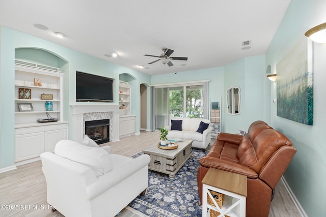living area featuring baseboards, a fireplace, a ceiling fan, light wood-type flooring, and built in shelves
