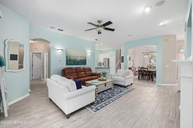 living area featuring arched walkways, a ceiling fan, light wood-style flooring, and baseboards