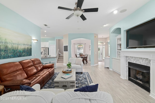living area featuring ceiling fan, light wood finished floors, stairs, a chandelier, and a fireplace