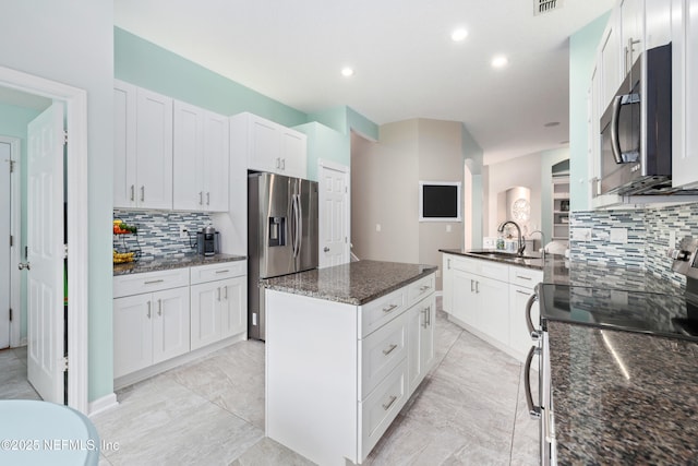 kitchen with stainless steel appliances, a sink, tasteful backsplash, a kitchen island, and dark stone counters