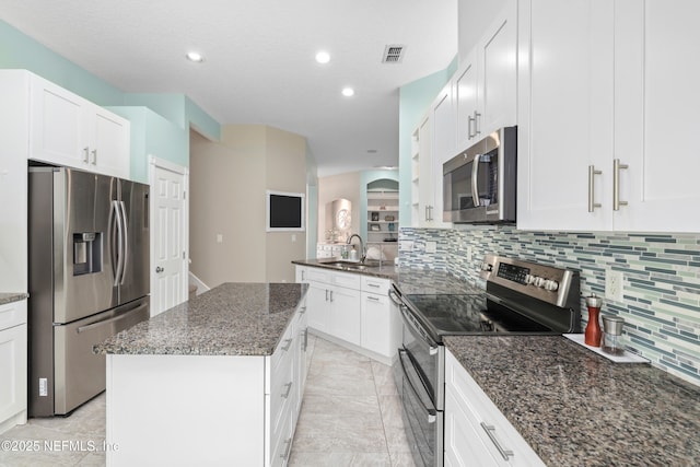 kitchen with appliances with stainless steel finishes, tasteful backsplash, a sink, dark stone counters, and a kitchen island