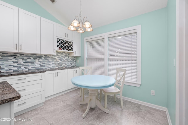 kitchen featuring tasteful backsplash, a chandelier, lofted ceiling, decorative light fixtures, and dark stone countertops