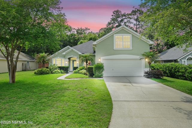 traditional-style home featuring a garage, driveway, a yard, and stucco siding