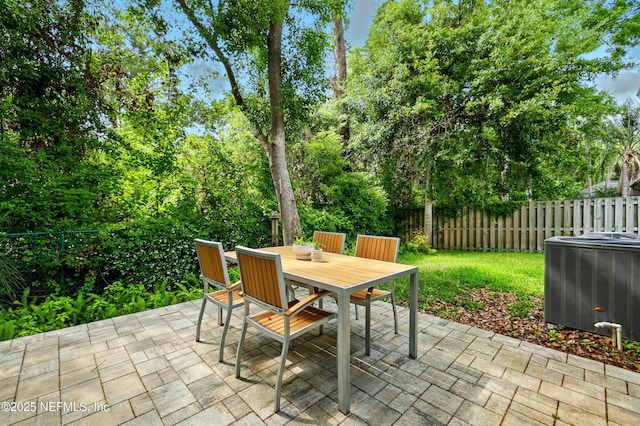 view of patio featuring cooling unit, a fenced backyard, outdoor dining space, and view of wooded area