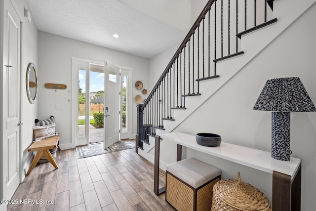 entrance foyer featuring a textured ceiling, baseboards, stairs, and wood finished floors
