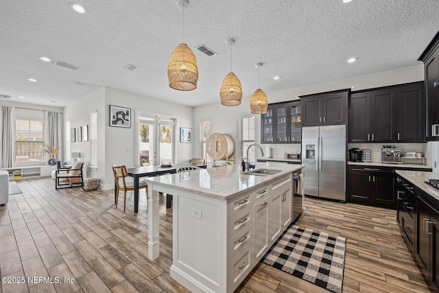 kitchen with visible vents, a breakfast bar, wood finished floors, a sink, and stainless steel refrigerator with ice dispenser