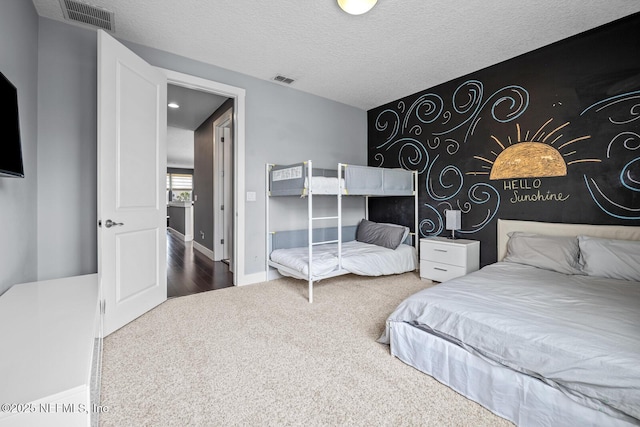 carpeted bedroom featuring visible vents, baseboards, an accent wall, and a textured ceiling