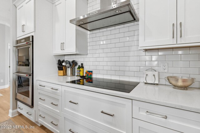 5698 Grand Cayman Rd, Jacksonville, FL 32226 - kitchen with light wood-style floors, white cabinetry, double oven, black electric stovetop, and exhaust hood