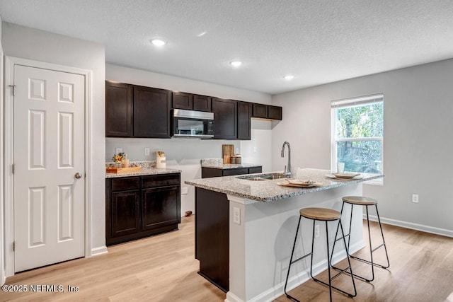 7829 Pipit Ave, Jacksonville, FL 32219 - kitchen featuring light wood-style flooring, an island with sink, a sink, dark brown cabinetry, and stainless steel microwave