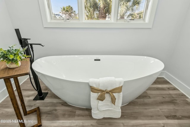 bathroom featuring a freestanding tub, baseboards, and wood finished floors