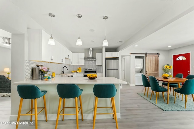 kitchen with a peninsula, stacked washer and dryer, appliances with stainless steel finishes, a barn door, and wall chimney range hood