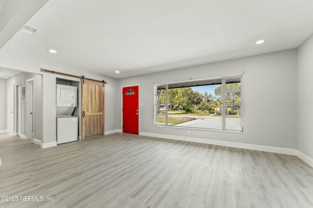 unfurnished living room with light wood finished floors, stacked washer and clothes dryer, baseboards, and a barn door