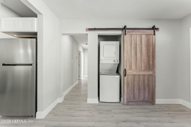 laundry area with baseboards, light wood finished floors, stacked washing maching and dryer, laundry area, and a barn door