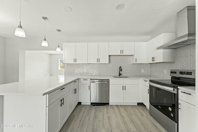 kitchen with wall chimney range hood, light countertops, appliances with stainless steel finishes, a peninsula, and a sink