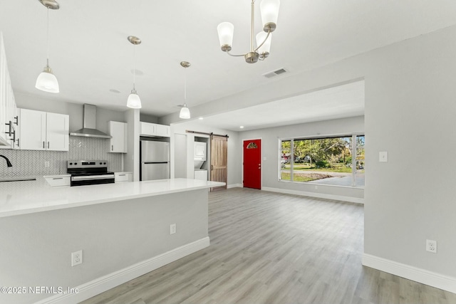 kitchen featuring a peninsula, appliances with stainless steel finishes, a barn door, wall chimney range hood, and backsplash