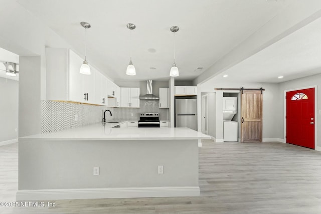 kitchen featuring stacked washer / dryer, a barn door, appliances with stainless steel finishes, wall chimney exhaust hood, and a sink