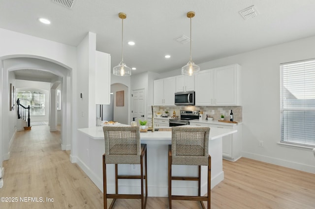 3852 Westridge Dr, Orange Park, FL 32065 - kitchen with a kitchen breakfast bar, backsplash, arched walkways, appliances with stainless steel finishes, and light wood finished floors