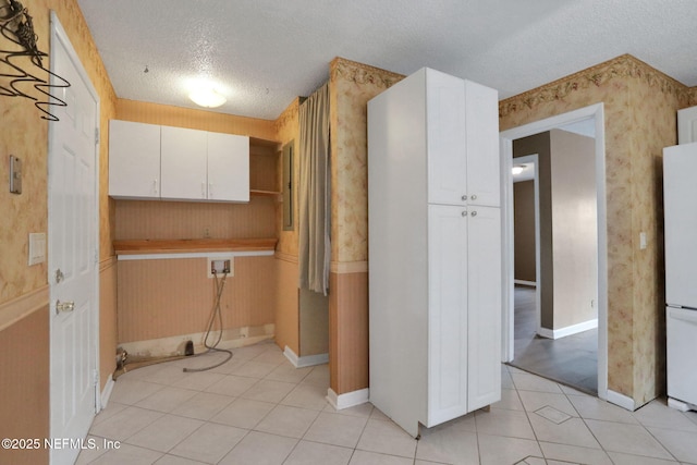 4245 New Hampshire Rd, Elkton, FL 32033 - kitchen featuring light tile patterned flooring, freestanding refrigerator, white cabinetry, a textured ceiling, and wallpapered walls