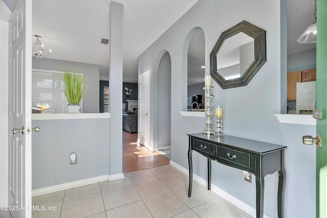 hallway featuring baseboards, visible vents, and light tile patterned floors