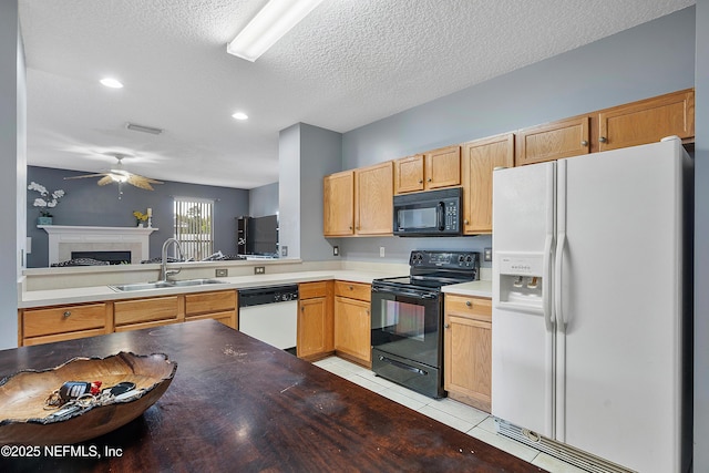 kitchen featuring a tile fireplace, a sink, light tile patterned floors, black appliances, and ceiling fan