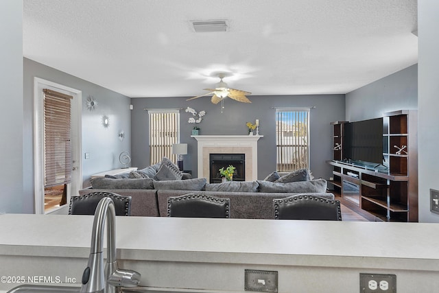 living room with a textured ceiling, visible vents, a fireplace, wood finished floors, and a ceiling fan