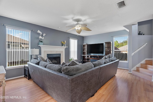 living area featuring a ceiling fan, light wood finished floors, a fireplace, baseboards, and visible vents