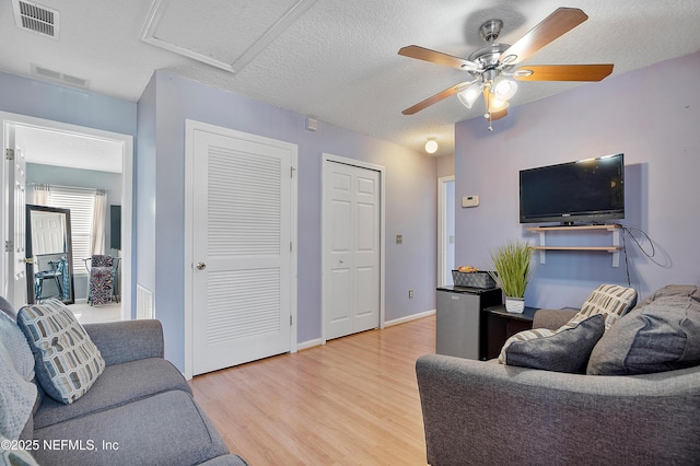 living room with a ceiling fan, visible vents, attic access, and wood finished floors