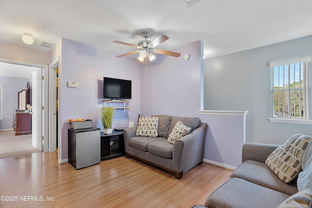 living room featuring a textured ceiling, visible vents, a ceiling fan, and light wood finished floors