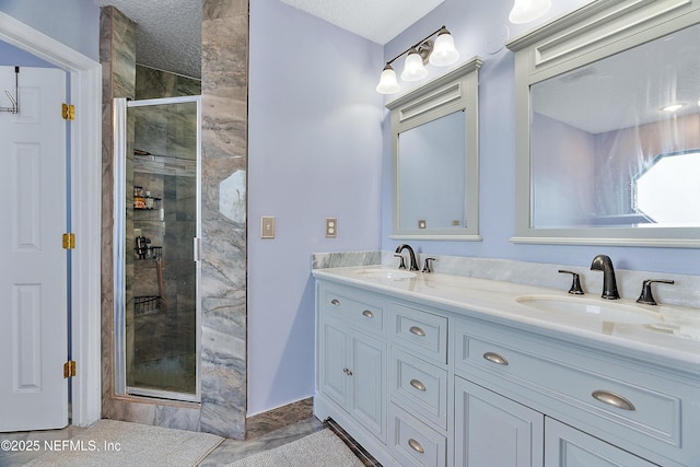full bath featuring a stall shower, double vanity, a sink, and a textured ceiling