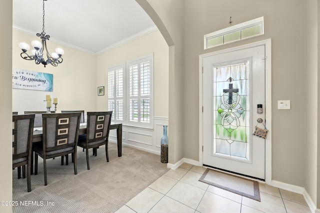 entrance foyer featuring ornamental molding, arched walkways, a chandelier, light colored carpet, and light tile patterned floors