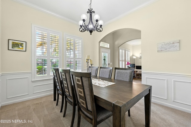 dining area with light carpet, ornamental molding, a decorative wall, healthy amount of natural light, and a wainscoted wall