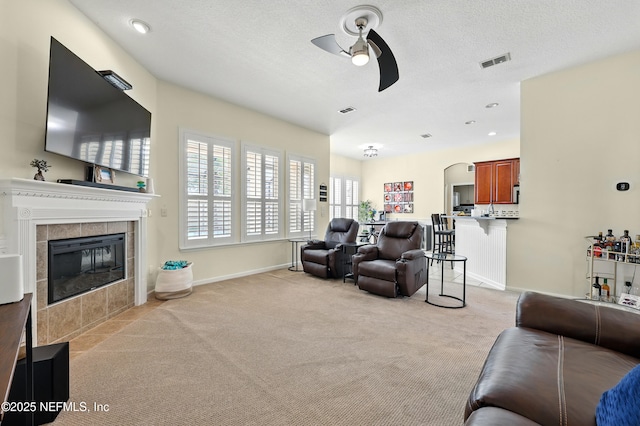 living room with a ceiling fan, light colored carpet, a tile fireplace, baseboards, and arched walkways