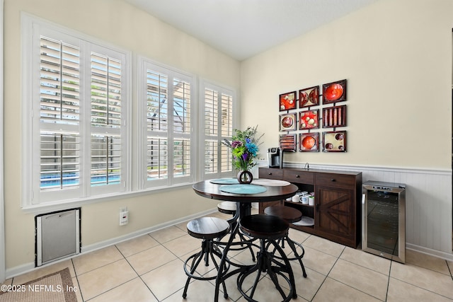dining area with wine cooler, light tile patterned floors, baseboards, and a wainscoted wall
