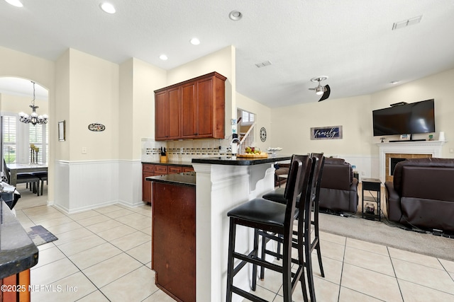 kitchen with dark countertops, a breakfast bar area, a wainscoted wall, a chandelier, and open floor plan