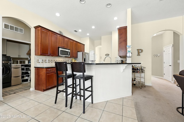 kitchen featuring appliances with stainless steel finishes, a kitchen breakfast bar, arched walkways, washer / clothes dryer, and dark countertops