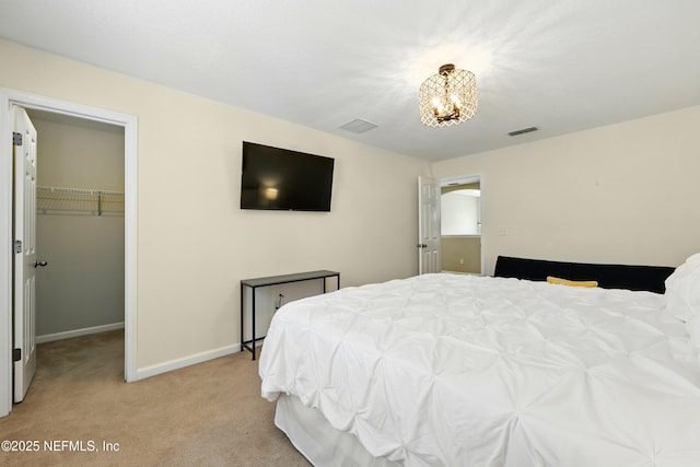 bedroom with light colored carpet, a chandelier, a walk in closet, baseboards, and a closet