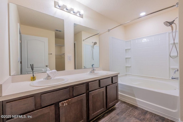 full bathroom with double vanity, a sink, washtub / shower combination, and wood finished floors