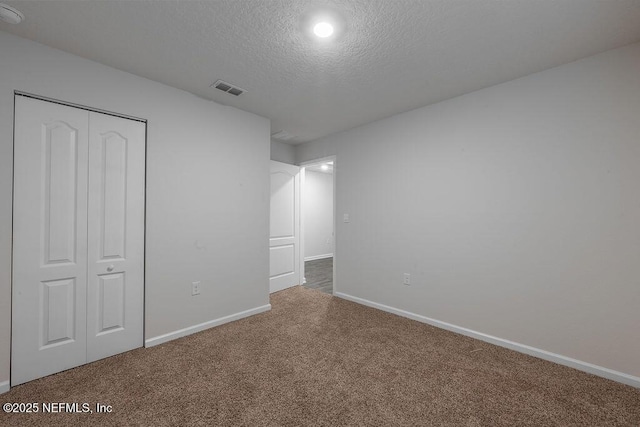unfurnished bedroom featuring baseboards, a textured ceiling, carpet floors, visible vents, and a closet