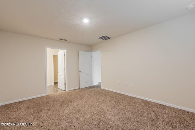 spare room with light carpet, a textured ceiling, baseboards, and visible vents
