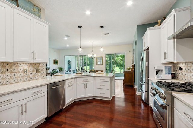 95150 Starling Ct, Fernandina Beach, FL 32034 - kitchen featuring appliances with stainless steel finishes, a sink, wall chimney range hood, a peninsula, and dark wood-type flooring
