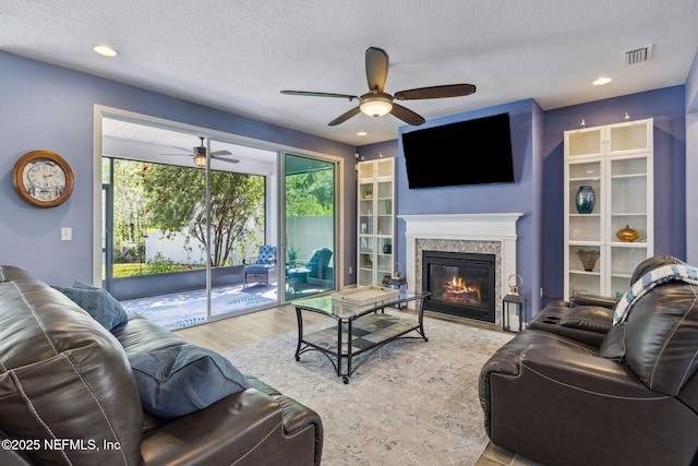 living room with a textured ceiling, visible vents, ceiling fan, wood finished floors, and a glass covered fireplace