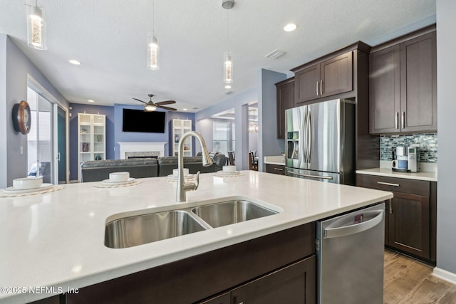 kitchen with a fireplace, ceiling fan, stainless steel appliances, dark brown cabinets, and a sink