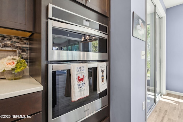 kitchen featuring light wood finished floors, double oven, light countertops, and dark brown cabinetry