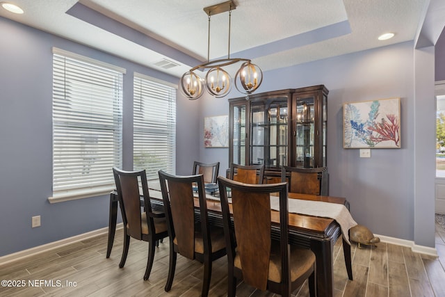 dining room with wood tiled floor, visible vents, an inviting chandelier, and a raised ceiling