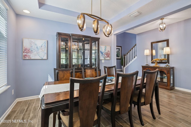 dining room featuring visible vents, a chandelier, baseboards, wood tiled floor, and a tray ceiling