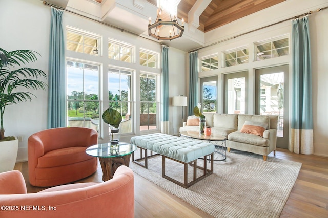 living room with coffered ceiling, a notable chandelier, beam ceiling, a high ceiling, and light wood-type flooring